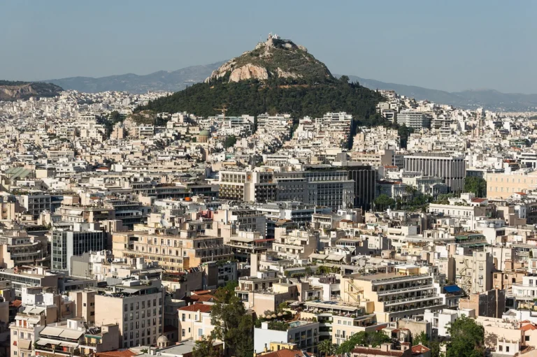 View over white city buildings to a tree-covered hill in Athens